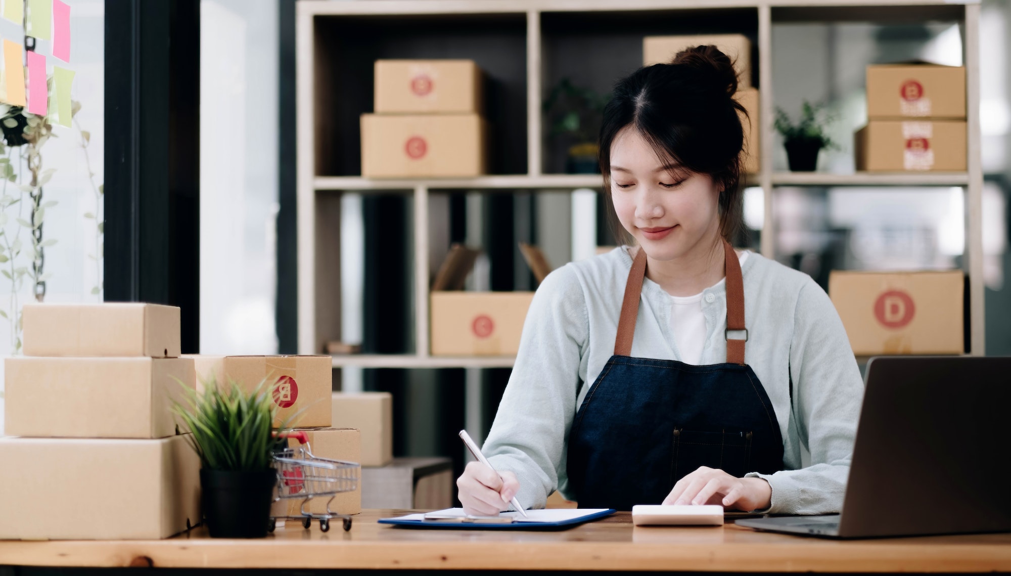 A portrait of a young Asian woman, e-commerce employee sitting in the office full of packages in the